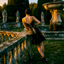 Back view of woman wearing black bandage dress with gold trim and tiered ruffle mermaid hem.