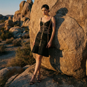 Woman leaning on a wall wearing black bandage dress with gold trim, sweetheart neckline and tiered ruffle mermaid hem.